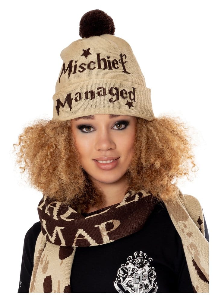 Beige gebreide muts met omslag, donkerbruine pompon, sterretjes en de tekst ‘Mischief Managed’. Gedragen door een model dat recht vooruit kijkt, met een beige-bruine sjaal en zwart shirt tegen een witte achtergrond.