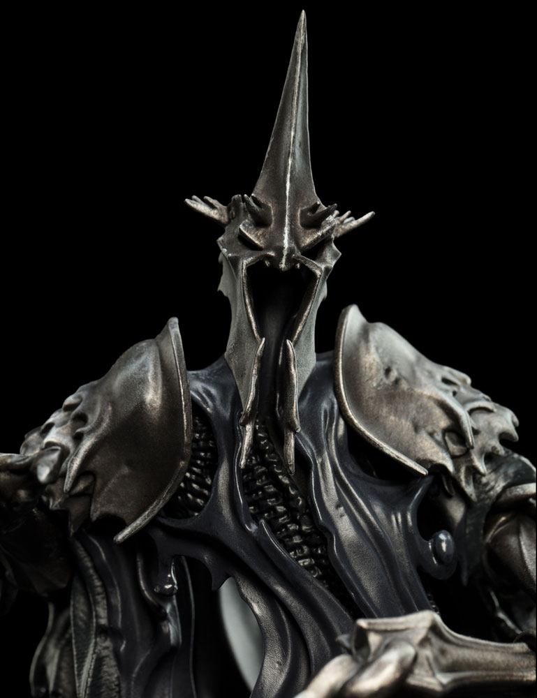 Close-up van een kunststof Witch-King-figuur, recht van voren, met zwarte mantel en metaalgrijs harnas. De hoge, puntige helm heeft een lege gezichtsopening; onderaan is een deel van het zwaard zichtbaar tegen een zwarte achtergrond.