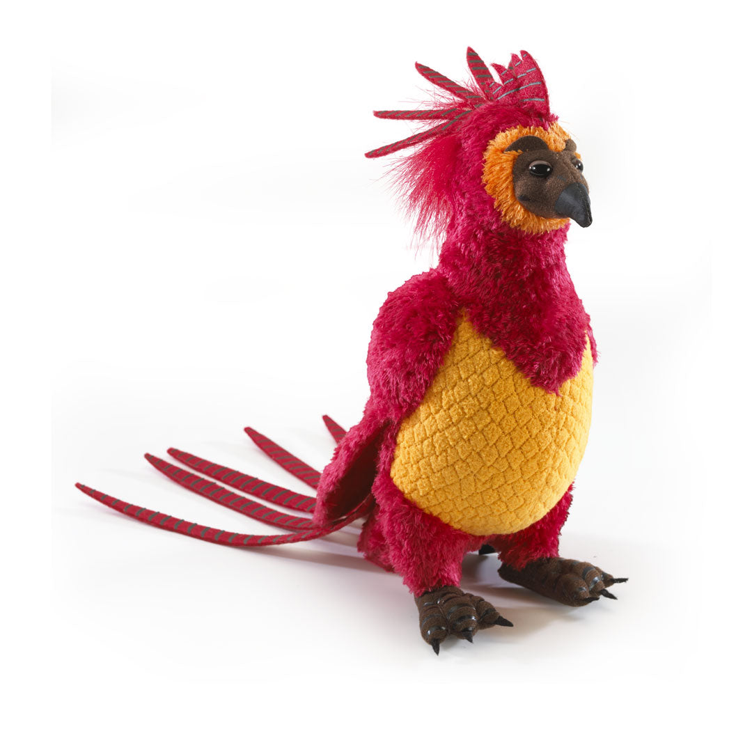 Pluchen knuffel van Felix de Feniks, rechtop en schuin naar rechts gedraaid op een witte achtergrond. Hij is rood met een gele buik, oranje gezichtskraag, donkere snavel en poten, een puntige kuif en lange staartveren.