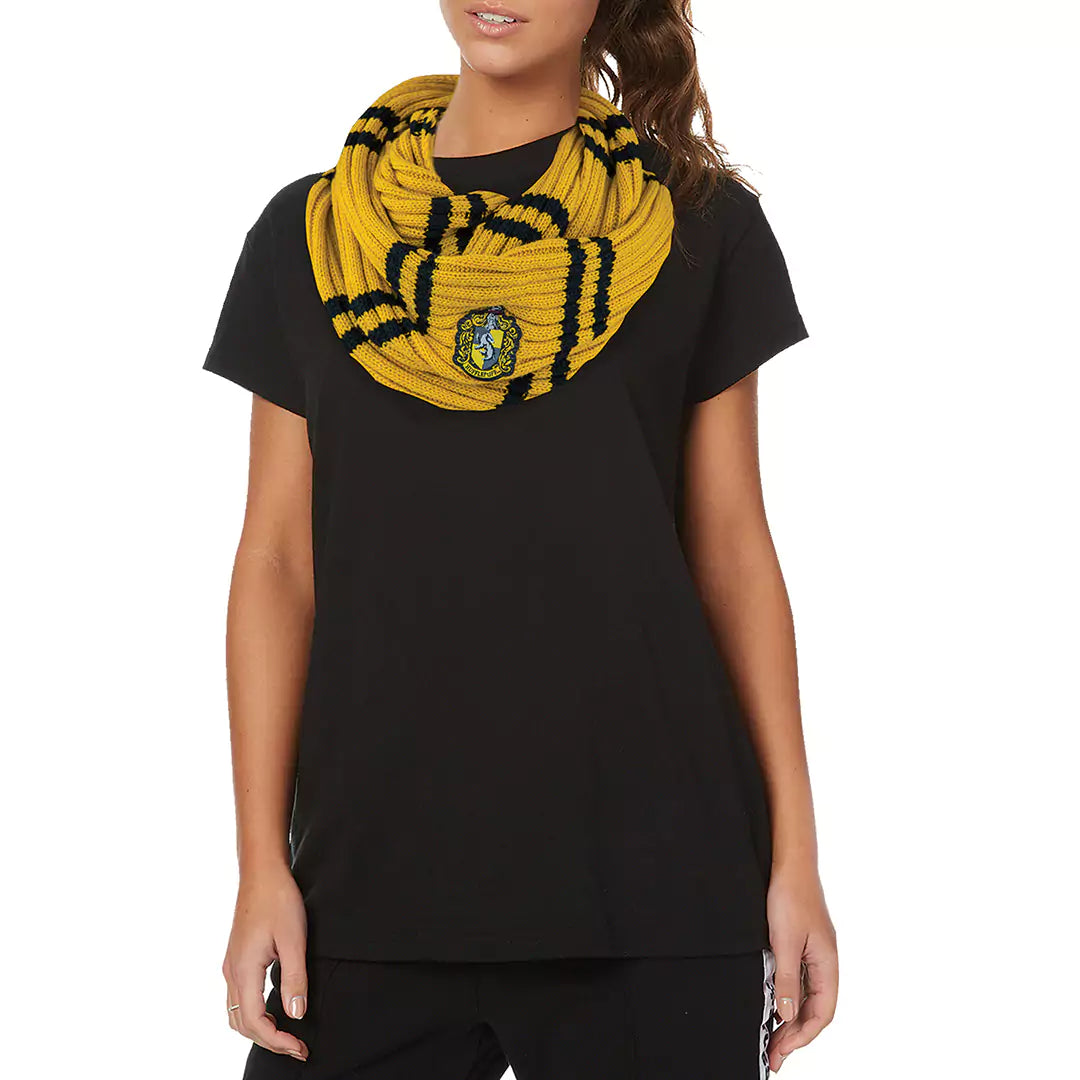 Gele, gebreide colsjaal met zwarte strepen en een Huffelpuf-wapen, in lussen om de hals van een model met een zwart T-shirt. Het model staat met de armen langs het lichaam tegen een witte achtergrond.