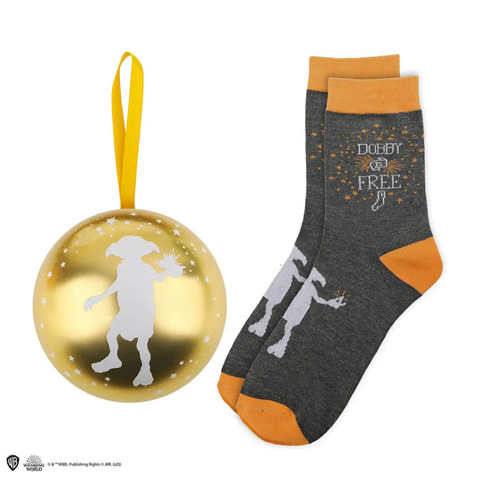 Twee overlappende donkergrijze gebreide sokken met oranje boorden, hielen en tenen en witte Dobby-silhouetten. Links ligt een glanzende goudkleurige bol met een wit Dobby-silhouet, sterren en een geel ophanglint, op een witte achtergrond.