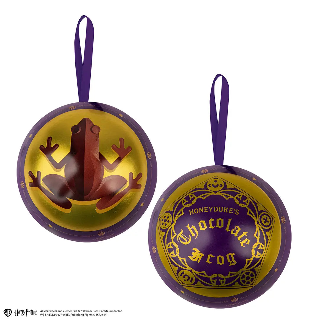 Twee aanzichten van een ronde, glanzende paars-gouden capsule met een paars stoffen ophanglint, tegen een witte achtergrond. Links staat een bruine kikker afgebeeld, rechts een sierlijk etiket met ‘Honeyduke’s Chocolate Frog’.