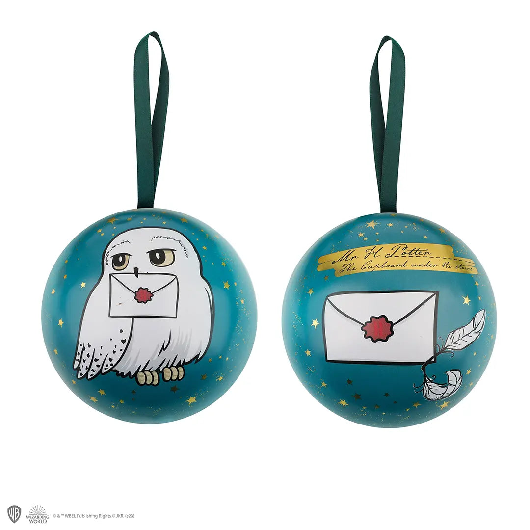 Twee aanzichten van een glanzende turquoise bol met gouden sterren en een donkergroene lintlus, tegen een witte achtergrond. De ene zijde toont de witte uil Hedwig met een brief in haar snavel, de andere een verzegelde envelop en veren.