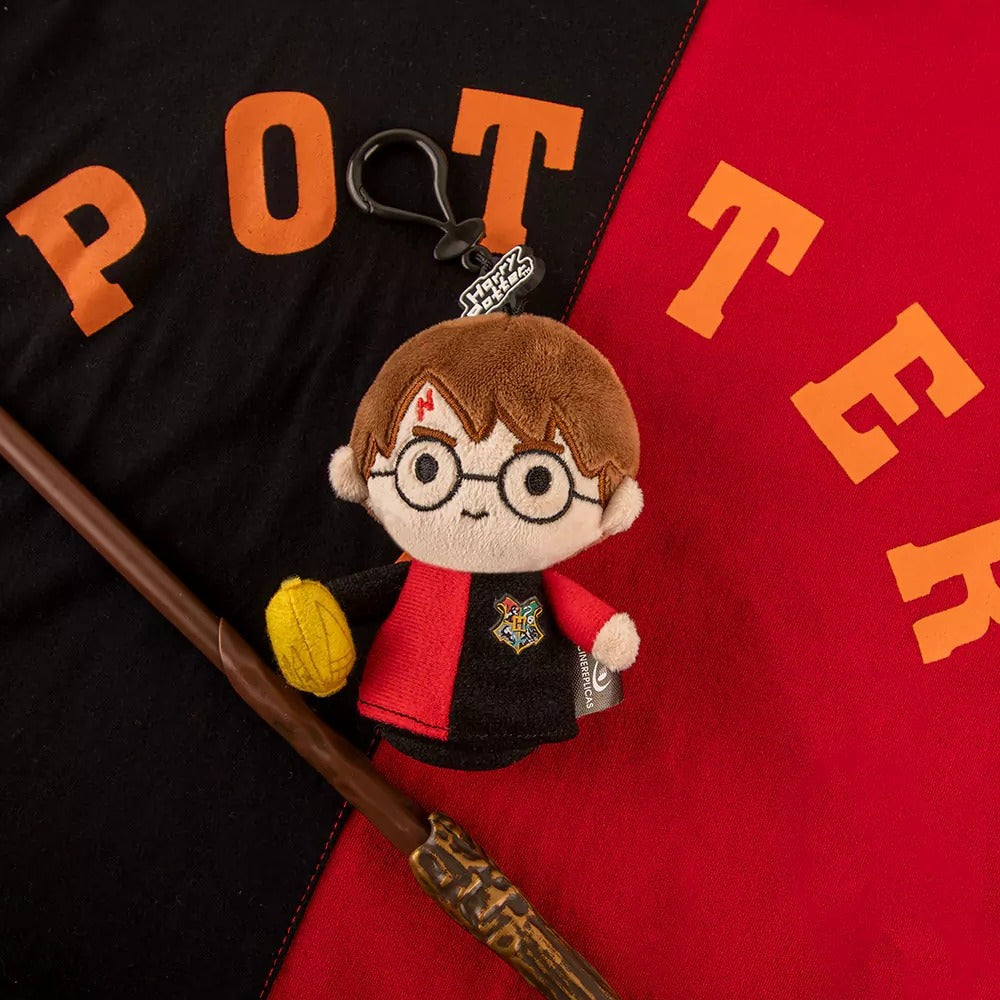 De Harry Potter-knuffelsleutelhanger met clip op een rood-zwart Potter-shirt, naast een toverstaf.