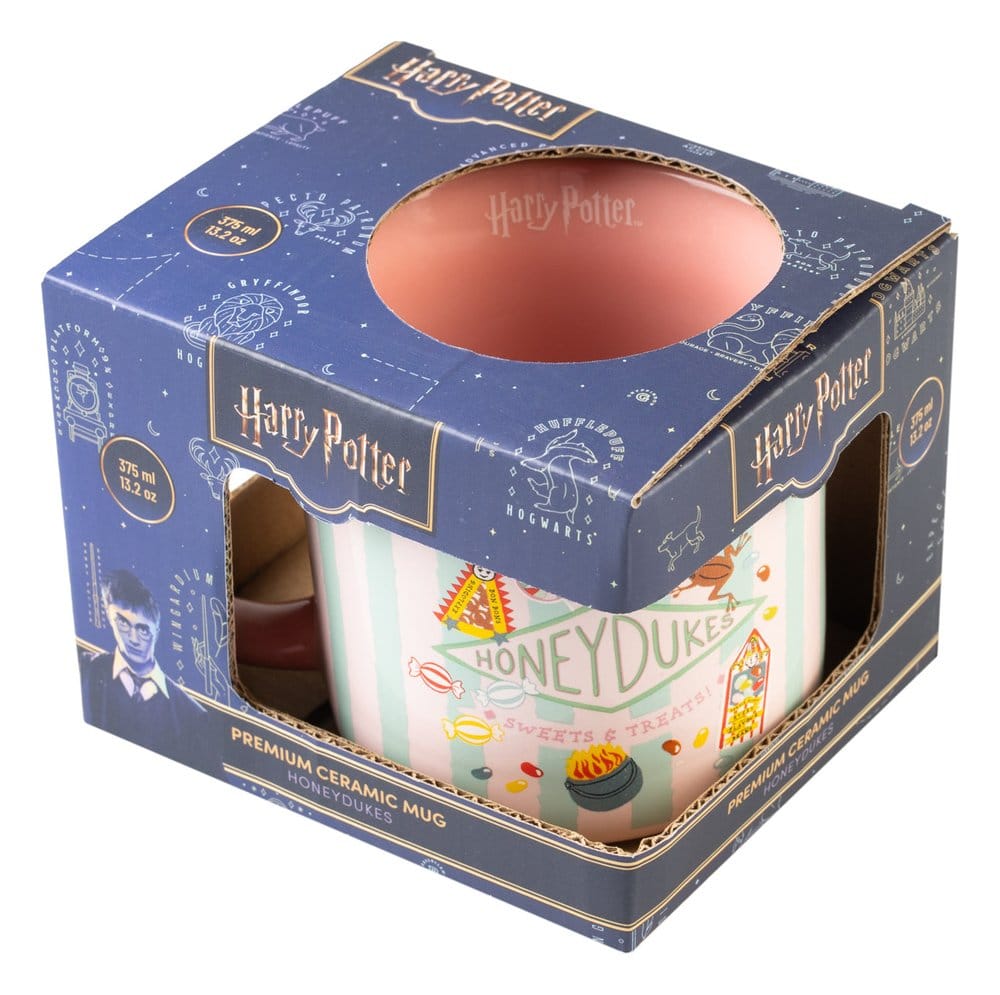 Keramische Honeydukes-mok met roze binnenkant, roze en mintgroene strepen en snoepillustraties. Schuin van boven gefotografeerd in een donkerblauwe kartonnen Harry Potter-doos met kijkvensters, tegen een witte achtergrond.