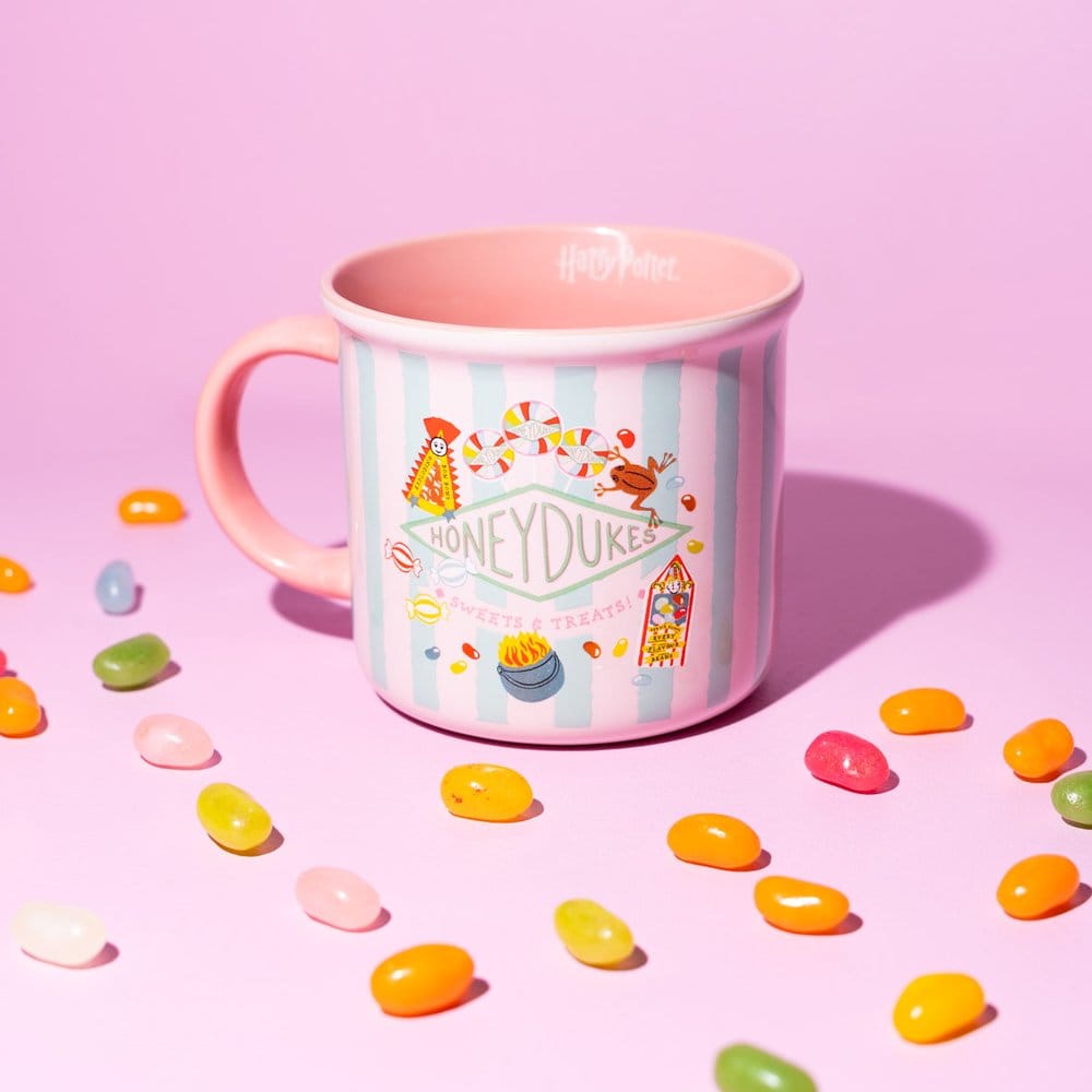 Glanzende keramieken mok met roze en mintgroene strepen, Honeydukes-logo en snoepillustraties. Het roze oor zit links; de mok staat tussen gekleurde snoepjes op een roze ondergrond tegen een roze achtergrond.