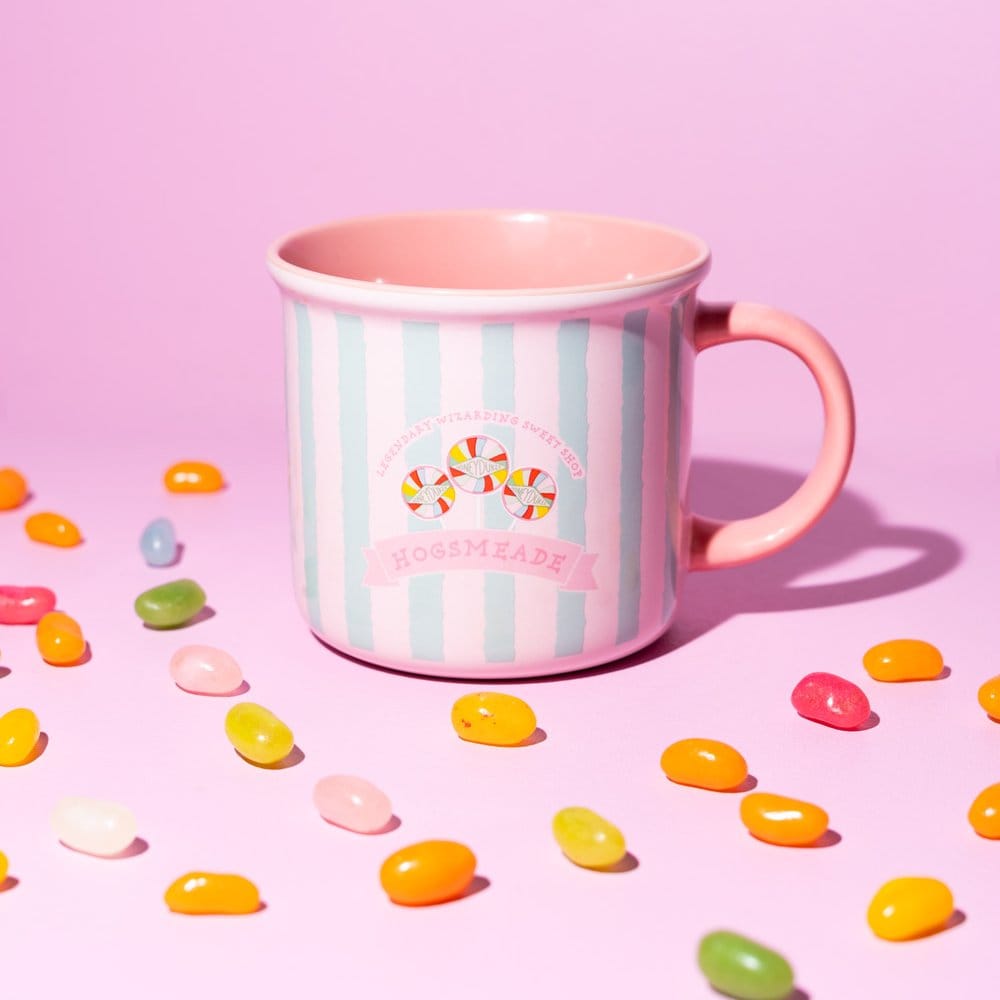 Glanzende keramische Honeydukes-mok met roze en lichtblauwe verticale strepen, snoepillustraties en een roze oor rechts. De mok staat op een roze ondergrond met gekleurde snoepjes, tegen een roze achtergrond.