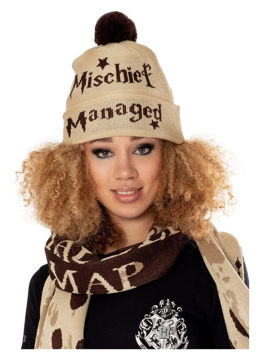 Beige gebreide muts met omslag, donkerbruine pompon, sterretjes en de tekst ‘Mischief Managed’. Gedragen door een model dat recht vooruit kijkt, met een beige-bruine sjaal en zwart shirt tegen een witte achtergrond.