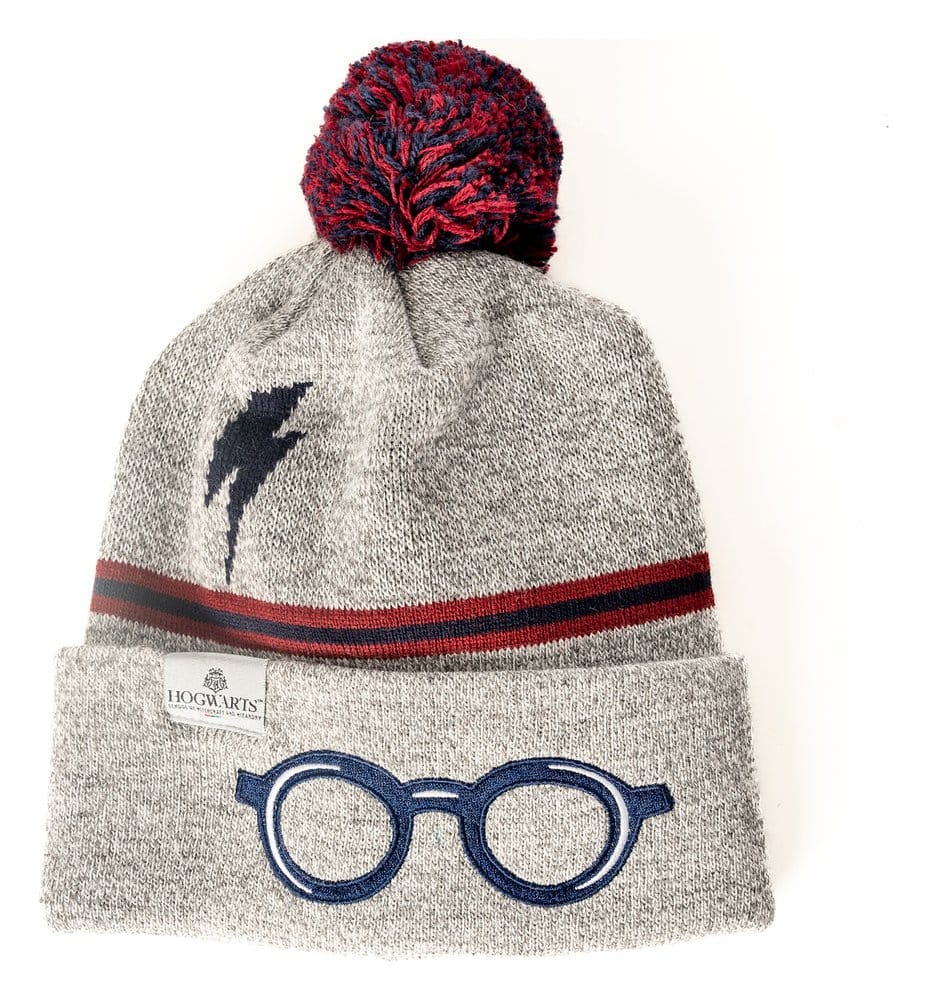 Grijze gebreide muts met rood-donkerblauwe pompon en strepen, een donkerblauwe bliksemschicht en een ronde bril op de omgeslagen rand. Vooraanzicht op een witte achtergrond, met een Hogwarts-label aan de rand.