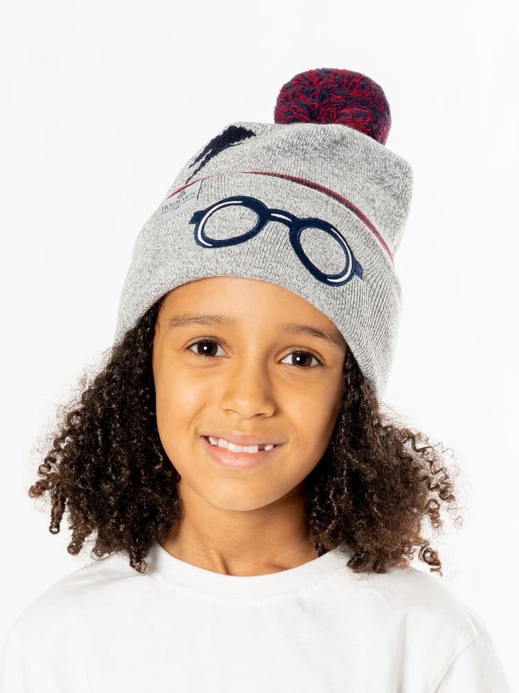 Een glimlachend kind draagt een grijze gebreide Harry Potter-muts met omgeslagen rand, donkerblauwe brilopdruk en rood-donkerblauwe pompon. Het kind kijkt recht vooruit en draagt een wit shirt tegen een witte achtergrond.